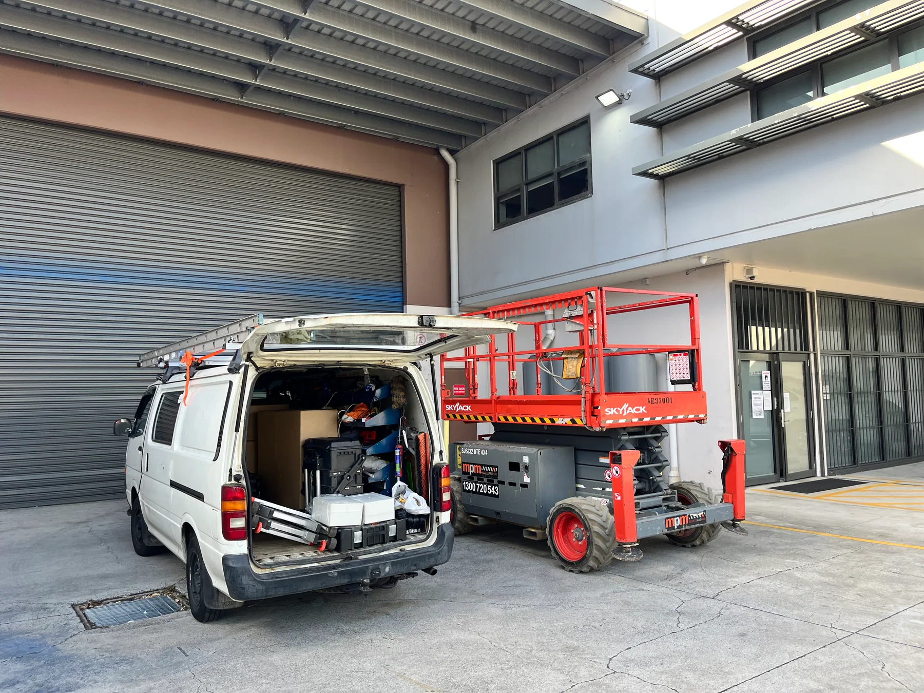 A work vehicle and scissor lift positioned beside a commercial building